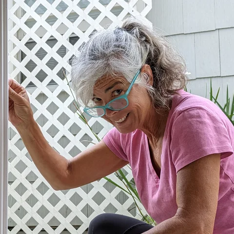 The author, smiling over her glasses while fixing a window with a screwdriver